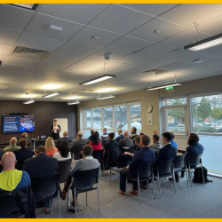 Image shows a meeting room where people are sat down listening to Kate Houlden from Like Technologies speak at the recent ElecTech event